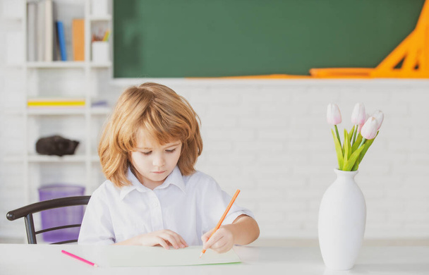 School kid writing in copybook and sitting at table in classroom. First grade. - Foto, Imagen