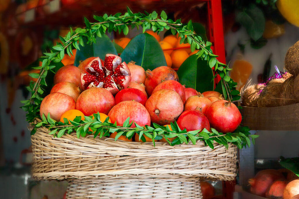 Cesta decorada con hojas verdes frescas con jugosas frutas maduras de granada y naranjas preparadas para exprimir jugo en un café callejero. - Foto, imagen