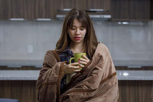 Woman with cold covered with a blanket at home, having a cup of coffee - Photo, Image
