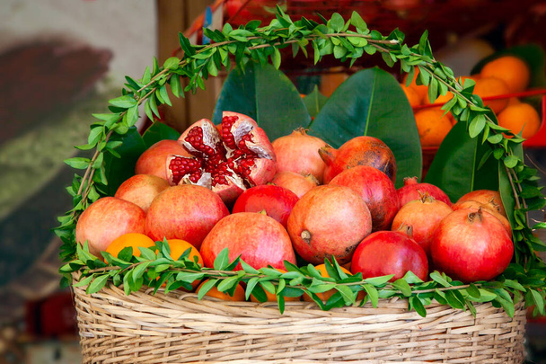 Košík zdobený čerstvě zelenými listy se šťavnatými zralými granátovými jablky ovoce a pomeranče připravenými pro vymačkání šťávy v pouliční kavárně. - Fotografie, Obrázek
