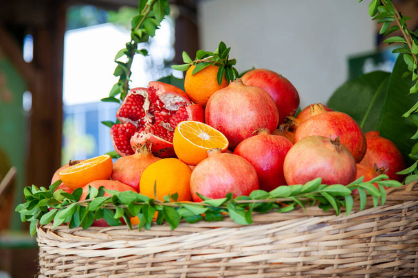Cesta decorada con hojas verdes frescas con jugosas frutas maduras de granada y naranjas preparadas para exprimir jugo en un café callejero. - Foto, imagen