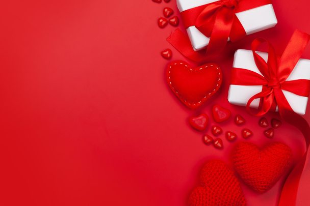 Valentijnsdag wenskaart sjabloon. Cadeaudoosjes, hartdecoratie en snoepjes over rode achtergrond. Bovenaanzicht plat lag met kopieerruimte - Foto, afbeelding