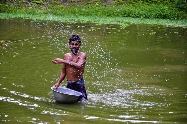 Un hombre tirando fertilizante al estanque por los peces. Un hombre adulto con un tazón grande flotando en el agua con fertilizante completo dando para que los peces se alimenten. El hombre a través del fertilizante - Foto, Imagen