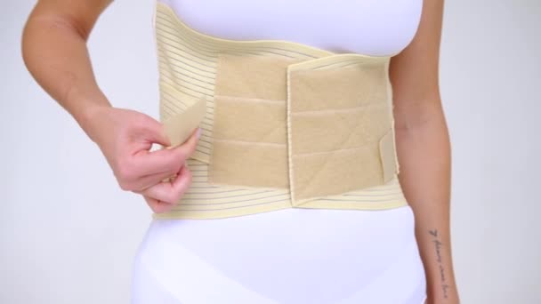 woman wearing beige support belt isolated on white. The girl fastens the belt - Felvétel, videó