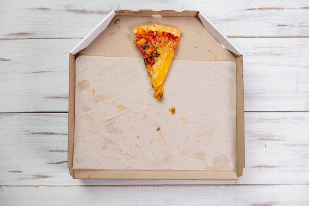 One last piece of pizza in a cardboard box. white wood background. Food concept. View from above. - Photo, image