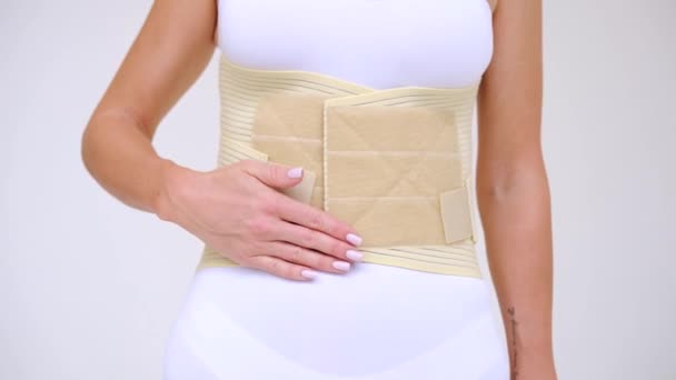 woman wearing beige support belt isolated on white. The girl demonstrates the belt to the camera and touches it with her hands - Footage, Video