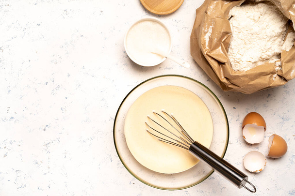 η διαδικασία παρασκευής ζύμης για τηγανίτες με συστατικά σε ένα ελαφρύ τραπέζι, αυγά και αλεύρι σαντιγί με ένα μίξερ - Φωτογραφία, εικόνα