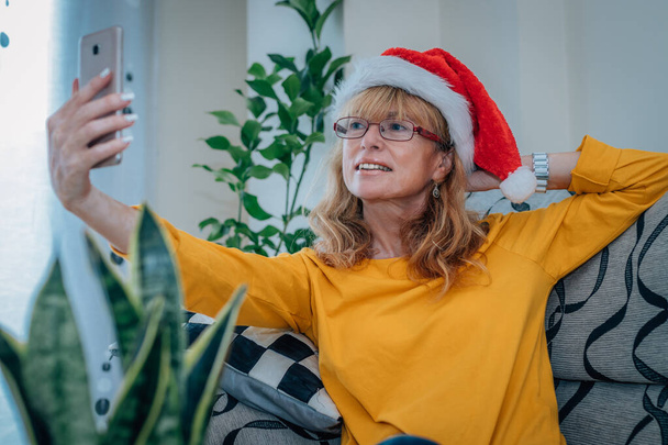 woman at home with santa claus hat talking on mobile phone on video or estreaming - Foto, Imagen