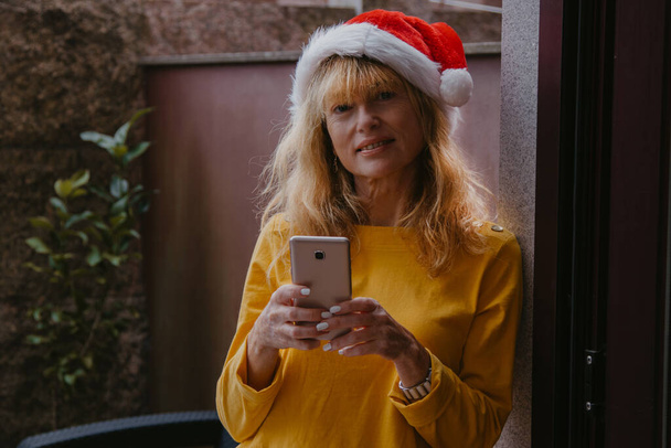 サンタ・クラスの帽子と携帯電話を持つ家の女性は - 写真・画像