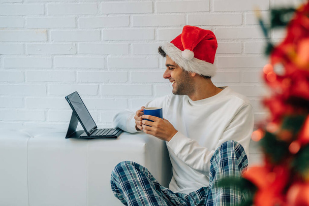 Noel Baba şapkalı adam evde dizüstü bilgisayarlı. - Fotoğraf, Görsel