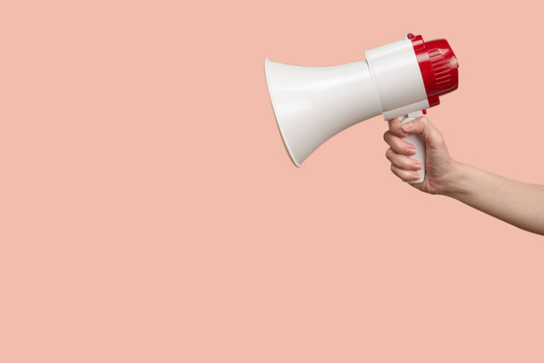 Megaphone in woman hands on a pink background. Copy space.  - Фото, изображение