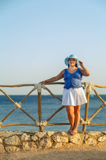 Young Jewish woman in a white skirt and blue hat on the seashore happy. - Foto, Bild