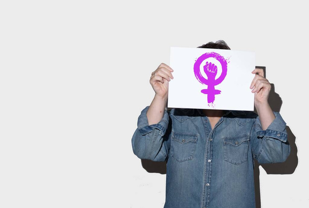 Unrecognizable woman on white background, holding a poster with feminist symbol.Feminism, feminist activism, International Women's Day, copy space - Foto, Imagen