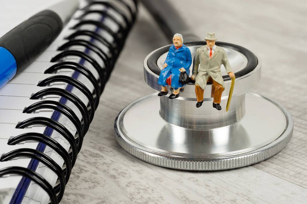 A conceptual image for elderly health care with a miniature couple sitting on a doctor's stethoscope - Фото, изображение