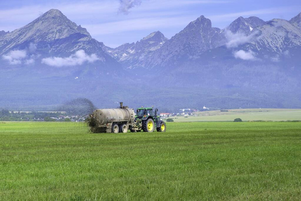 高いタトラ山脈の牧草地や畑で収穫を改善するために肥料を広げる大きなトラクター。農業の概念  - 写真・画像