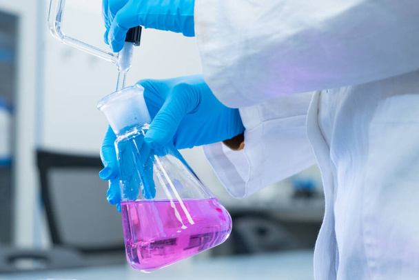 Close up scientist uses a titration method of analysis to study chemical properties of the water sample. Scientist holding Erlenmeyer flask with pink solution.  - Fotó, kép