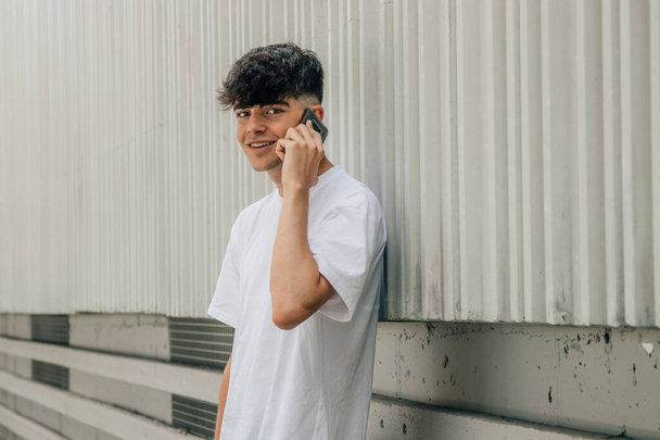 portret tiener jongen praten op mobiele telefoon op straat muur - Foto, afbeelding