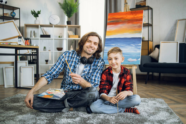 Father and son sitting on floor near colorful easel - Valokuva, kuva