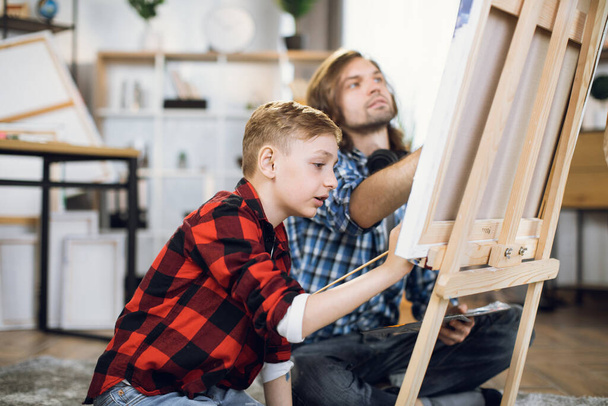 Father teaching son to draw with brush on easel - Valokuva, kuva