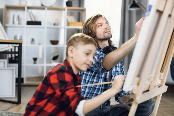 Caucasian boy and his father painting with brushes on easel - Photo, image