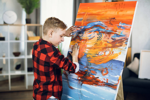 Inspired boy creating his masterpiece on easel with hands - Φωτογραφία, εικόνα