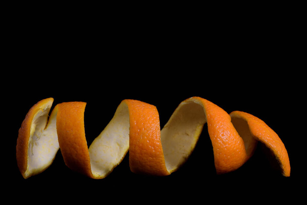 Close-up of the peel of a freshly peeled orange, which is curling up in a spiral and lying in front of a dark background - Photo, Image