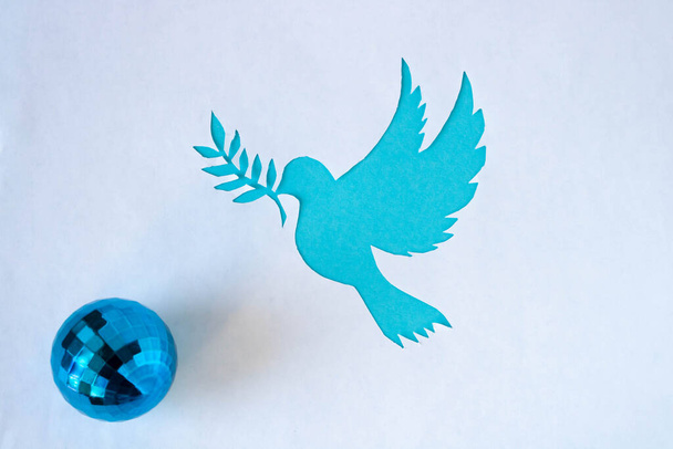 A dove stencil with a twig, cut out of white paper on a blue background for World Peace Day. World Science Day for Peace and Development. - Фото, изображение