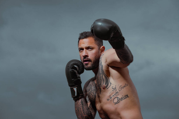Boxer in a fight. Fist fight. Strong man with tattooed body boxing outdoor. Man with muscular body and bare torso with boxing punch gloves. Sexy boxing man. - Foto, afbeelding