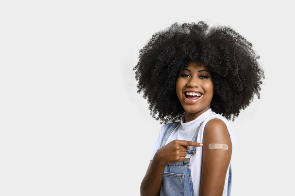 black teenage girl points to sticker on her arm showing she was vaccinated, isolated on gray background. - Fotografie, Obrázek