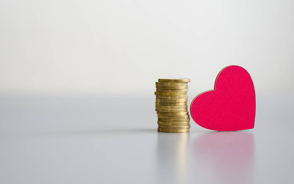 Stack of coins and a wooden red heart on a gray background. Donation concept. - Photo, Image