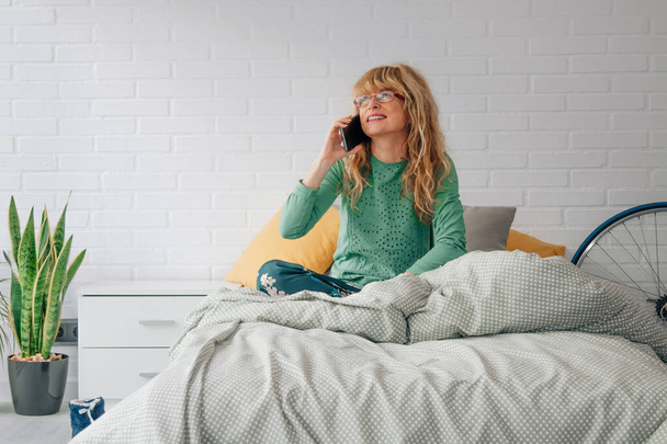 vrouw thuis in slaapkamer praten op mobiele telefoon - Foto, afbeelding