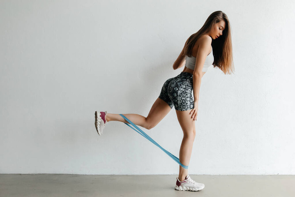 Крупный план спортивных упражнений с резинкой сопротивления для тонуса тела, в спортивной одежде и кроссовках - Фото, изображение