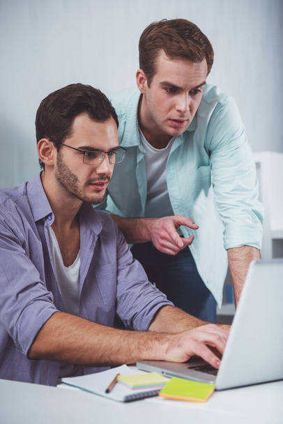 Two young attractive businessmen in casual clothes using laptop while working in office - Photo, Image