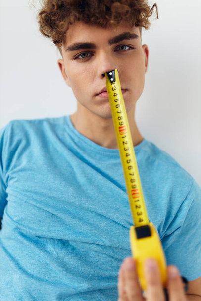 handsome guy yardstick in hand in blue t-shirts isolated background - Foto, Imagen