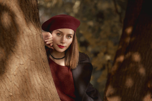 Close up portrait of young woman with high fashion look, leaning against a tree at the woods, looking at camera - Fotó, kép
