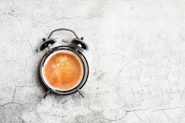 Bell alarm clock with a cup of coffe in clock face on a marble background with copy space - Fotoğraf, Görsel