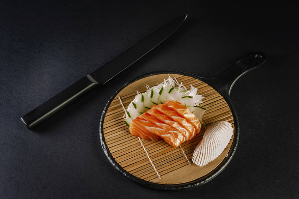 Salmon sashimi with a black knife on a black background. - Foto, Imagem