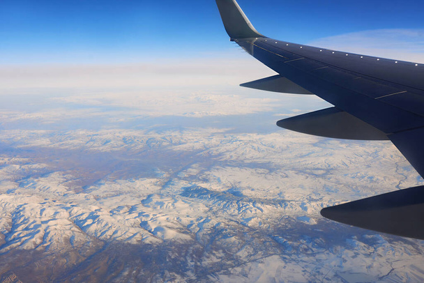 View to the wing of airplane in the sky and snowy mountains. Travel and transportation concept - Foto, Bild