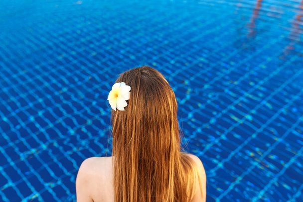 retro della donna caucasica con i capelli di log e fiore in esso seduto sul bordo della piscina. Viaggi, benessere, benessere, sport, chill concept  - Foto, immagini