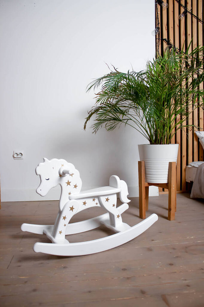 Children's rocking horse with stars. A flower on the floor. Against the background of a white wall. - Fotó, kép