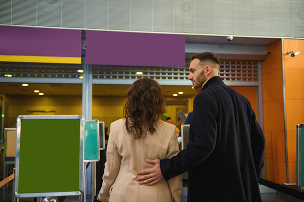 Rear view of a young multiracial couple of business partners standing at the check-in counter while waiting for check-in, customs and passport control at the airport terminal. Copy space - Photo, image