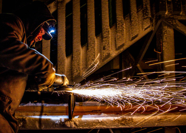 A man grinding metal in the cold and in the dark with winter gear on - Fotoğraf, Görsel