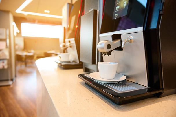 Крупним планом професійні кавові машини самообслуговування в залі ресторану та зоні очікування терміналу відправлення аеропорту. Сонячні промені падають в приміщенні під час заходу сонця
 - Фото, зображення