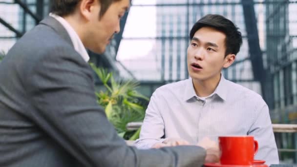 dos asiático negocios personas sentado en al aire libre café tienda tener un discusión - Metraje, vídeo