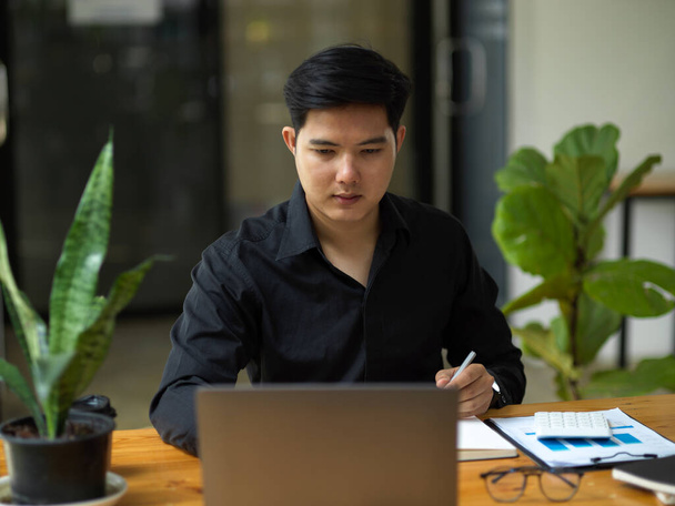 Розумний азіатський молодий бізнесмен, який працює на ноутбуці на своєму сучасному робочому місці
. - Фото, зображення