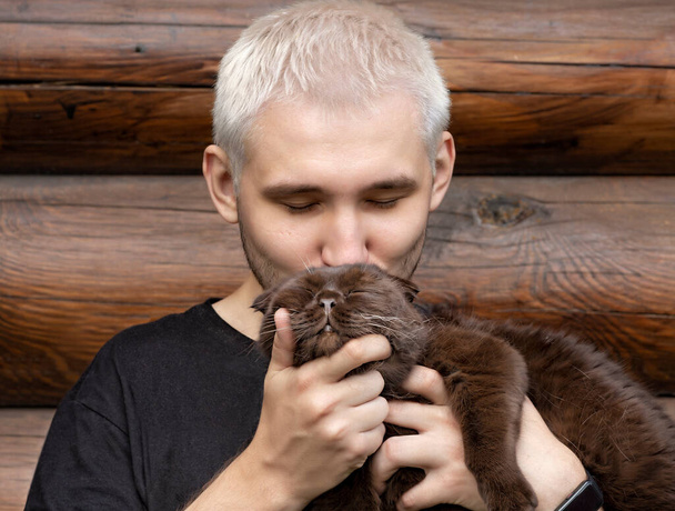 Un giovane ragazzo bacia il suo gatto appagato tenendolo tra le braccia - Foto, immagini