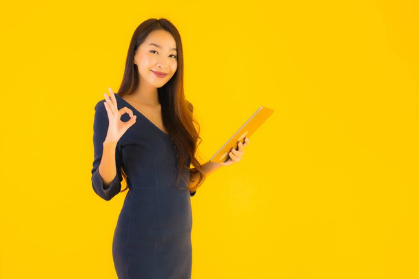 Portrait beautiful young asian woman with smart tablet electronic on yellow isolated background - Photo, Image