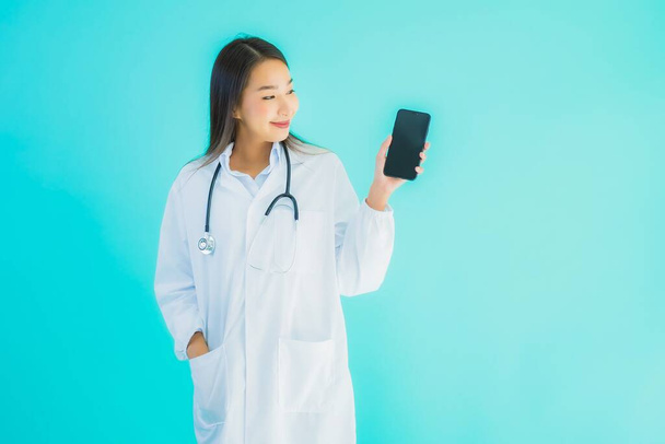 Portrait beautiful young asian doctor woman use mobile smart cell phone for clinic or hospital on blue isolated background - Photo, Image