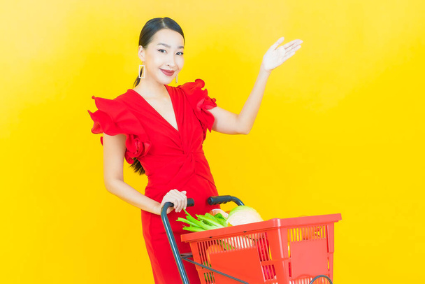 Portrait beautiful young asian woman smile with grocery basket from supermarket on color background - Fotó, kép