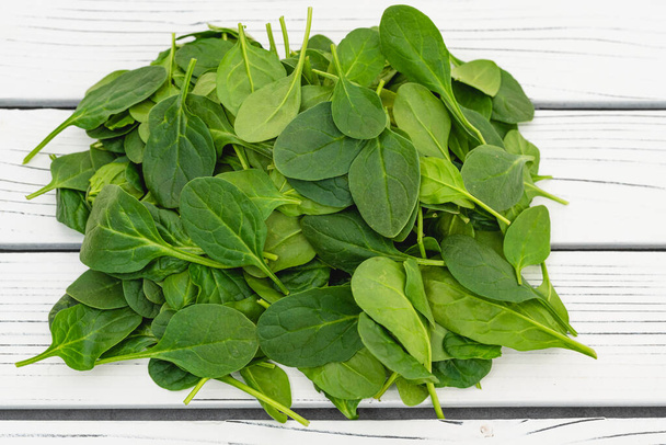Baby spinach leaves close up on white wooden board, flat lay with copy space - 写真・画像